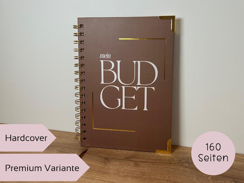 May include: A brown hardcover budget planner with gold accents and spiral binding. The cover features the words "mein BUDGET" in white. The planner has 160 pages.