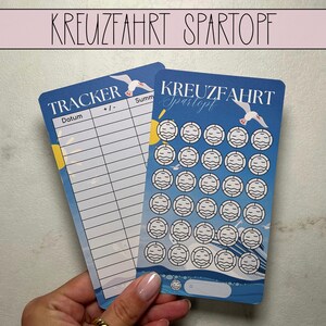 Puede incluir: Dos tarjetas azules con texto en alemán, "KREUZFAHRT SPARTOPF" en la parte superior. Una tarjeta tiene un rastreador con líneas para fechas y un gráfico de gaviota. La otra tarjeta tiene círculos con gráficos de barcos y una gaviota. Las tarjetas son sostenidas por una persona.