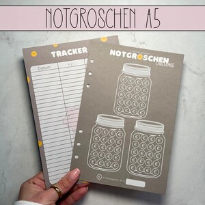 Może przedstawiać: Szary i biały drukowalny tracker do oszczędzania monet. Tracker zawiera sekcję do rejestrowania dat i zapisanych kwot. Tracker zawiera również sekcję z trzema słoikami, każdy z 100 kółkami reprezentującymi monety. Tekst "NOTGROSCHEN CHALLENGE" znajduje się na górze trackera.