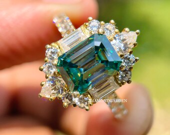 May include: A gold ring with a large emerald green square-shaped gemstone surrounded by smaller diamonds. The ring has a delicate band with smaller diamonds.