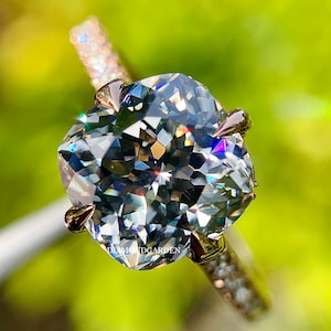 May include: A silver engagement ring with a large, cushion-cut diamond. The diamond is set in a prong setting and has a lot of sparkle. The band is set with smaller diamonds.