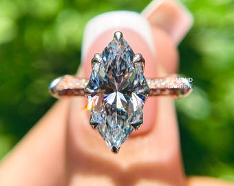 May include: A marquise-cut diamond ring with a rose gold band. The diamond is clear and faceted, reflecting light. The band has small, sparkling accents. The text "DIAMOND GARDEN" is visible on the band.