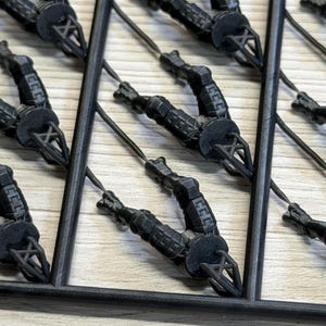 以下が含まれることがあります： 複数の同一のミニチュアフィギュアを含む黒いプラスチック製のスプルーフレーム。各フィギュアは脚を曲げた座った姿勢で成形されており、細いプラスチックの接続部でフレームに取り付けられています。フィギュアにはセグメント化されたアーマーのディテールが施されています。