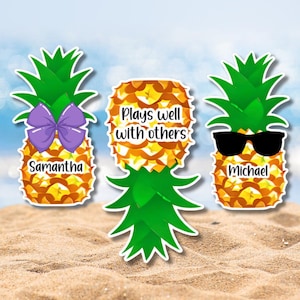 May include: Three pineapple-shaped cutouts with green leaves and yellow textured bodies. The left pineapple has a purple bow and the name Samantha. The center pineapple features the text Plays well with others. The right pineapple wears black sunglasses and the name Michael.