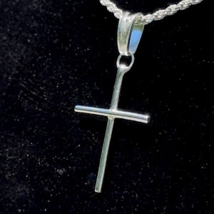 May include: A silver rope chain necklace with a silver cross pendant. The necklace is displayed on a black velvet background.
