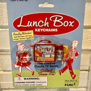 May include: A packaged Lunch Box keychain set. The red and white package features a miniature lunchbox, thermos, and toy snack. The text reads "Lunch Box Keychains" and "Collect Them All!" The set is for ages 8 and up.