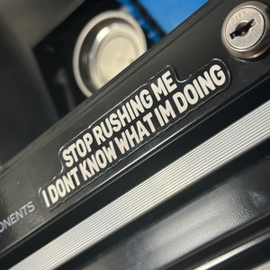 Może przedstawiać: Czarna metalowa skrzynka narzędziowa z srebrną naklejką z napisem "STOP RUSHING ME I DON'T KNOW WHAT I'M DOING".