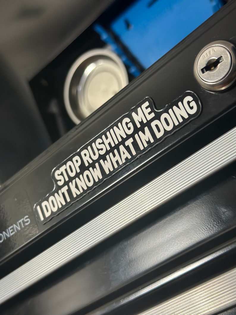 Może przedstawiać: Czarna metalowa skrzynka narzędziowa z srebrną naklejką z napisem "STOP RUSHING ME I DON'T KNOW WHAT I'M DOING".