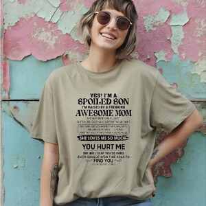 K&ouml;nnte beinhalten: Hell olivgr&uuml;nes T-Shirt mit dem Text "YES! I'M A SPOILED SON I'M RAISED BY A FREAKING AWESOME MOM" in Schwarz. Das Shirt hat einen Rundhalsausschnitt und kurze &Auml;rmel. Das Shirt ist aus weichem Material.