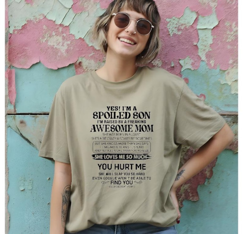 K&ouml;nnte beinhalten: Hell olivgr&uuml;nes T-Shirt mit dem Text "YES! I'M A SPOILED SON I'M RAISED BY A FREAKING AWESOME MOM" in Schwarz. Das Shirt hat einen Rundhalsausschnitt und kurze &Auml;rmel. Das Shirt ist aus weichem Material.