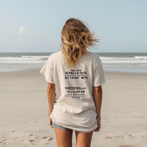 K&ouml;nnte beinhalten: Hellbeige T-Shirt mit schwarzem Text auf dem R&uuml;cken. Der Text lautet: "YES! I'M A SPOILED SON IN RAISED BY A FREAKING AWESOME MOM SHE LOVES ME SO MUCH YOU HURT ME EVEN GOOGLE CAN'T EASILY FIND YOU". Die Person steht am Strand.