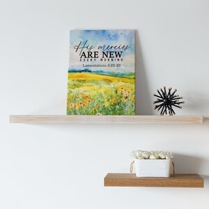 May include: A watercolor painting of a field of flowers with a blue sky in the background. The text "His mercies are new every morning" and "Lamentations 3:22-23" are printed on the painting.