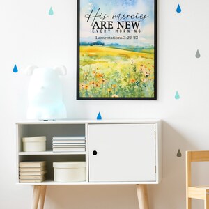 May include: A framed watercolor print with a quote about God's mercies being new every morning. The quote is from Lamentations 3:22-23. The print is hanging on a white wall with blue and gray raindrops.