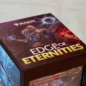 May include: A brown card storage box with the words "EDGE OF ETERNITIES" in yellow and white. The box features a fantasy illustration with the "MAGIC" logo. The bottom of the box shows a card with the text "Szarel, Genesis Shepherd".