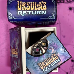 May include: A blue box with the words "Ursula's Return" on the top. The box is open and a game board with a spinning wheel is visible. The game board has a purple and blue background with the words "Ursula's Return" on it.
