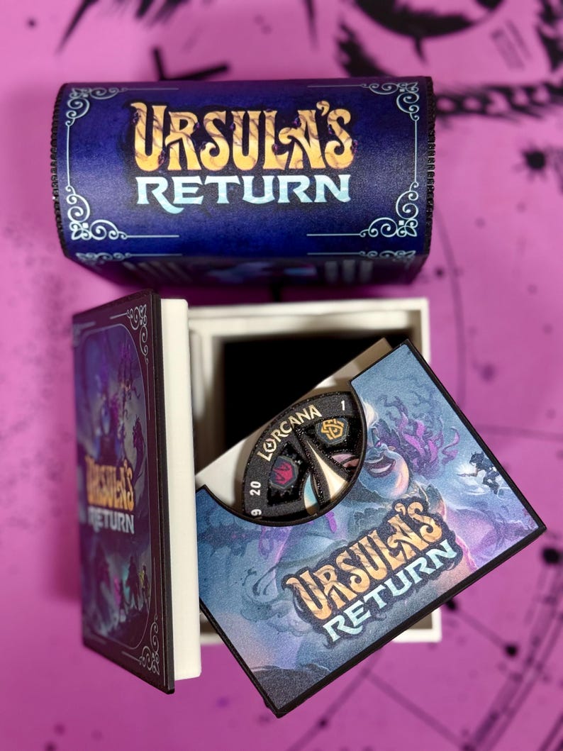 May include: A blue box with the words "Ursula's Return" on the top. The box is open and a game board with a spinning wheel is visible. The game board has a purple and blue background with the words "Ursula's Return" on it.