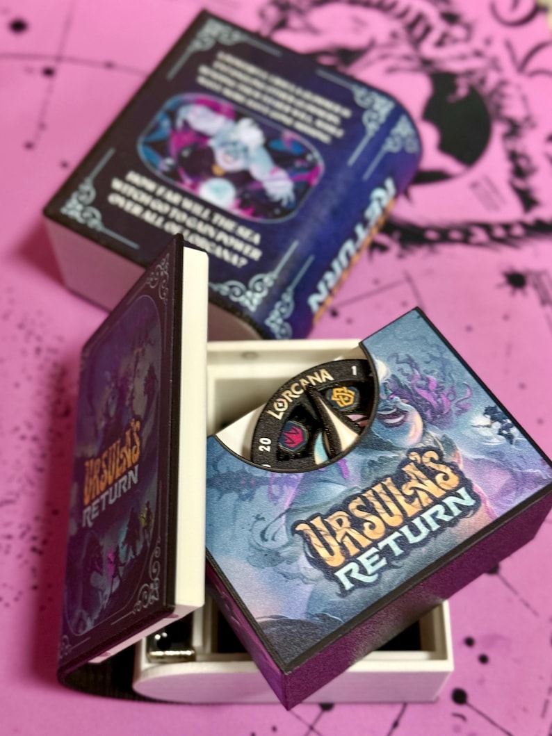 May include: A closed box with a blue and purple design featuring the text "Ursula's Return". The box is open to reveal a smaller box with a black and white spinning wheel with the text "Lorcaana" and "20".