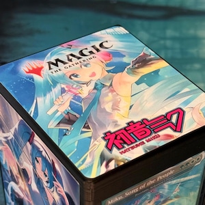 Könnte beinhalten: Eine quadratische Deckbox mit Hatsune Miku-Grafiken auf der Oberseite und den Seiten. Die Oberseite zeigt das Magic The Gathering-Logo, eine blauhaarige Figur mit Mikrofon sowie den Text Hatsune Miku in pinkfarbenen japanischen und englischen Schriftzeichen.