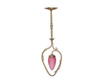 May include: Antique brass pendant light with a pink glass shade. The light fixture has an ornate design with a decorative ceiling mount and a curved frame. The pink glass shade has a textured pattern.