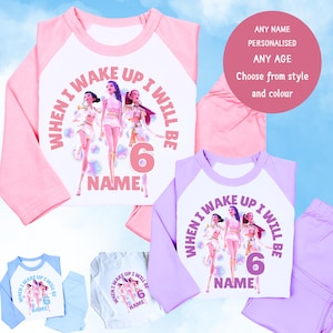 May include: A selection of children's pyjama sets in pink, blue, white, and lavender. Each set features a graphic of three figures and the text "WHEN I WAKE UP I WILL BE 6 NAME". A pink circle reads "ANY NAME, PERSONALISED, ANY AGE, Choose from style and colour".