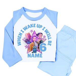 May include: A light blue and white pajama set with a graphic featuring three animated figures and the text "WHEN I WAKE UP I WILL BE 6 NAME". The set includes a long-sleeved top and matching pants.