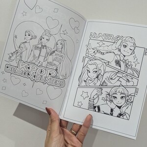 Op de afbeelding: Open kleurboek met zwart-wit illustraties van personages in anime-stijl. De cover leest "KPOP Demon Hunters". Binnenpagina's tonen gedetailleerde tekeningen met tekst.