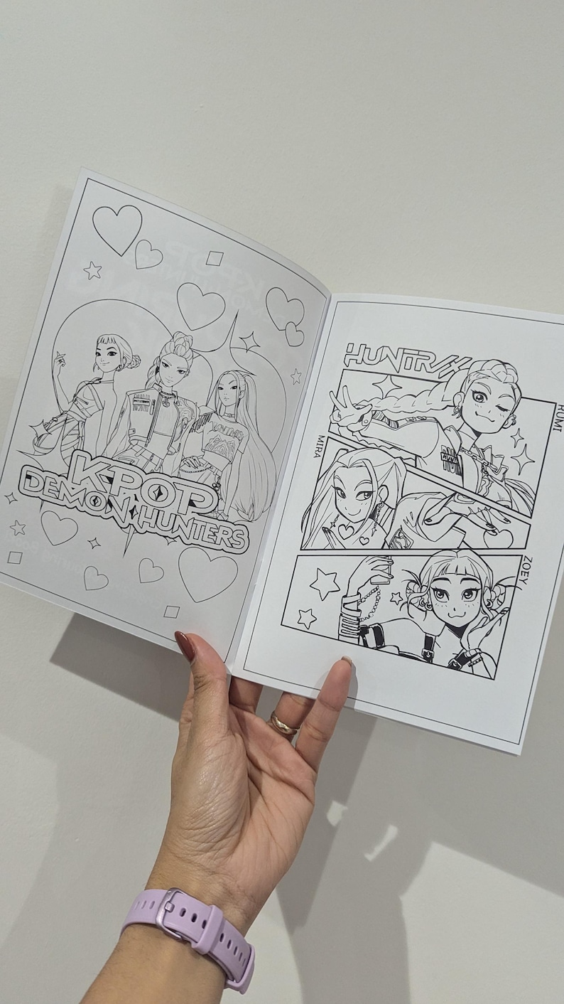 Op de afbeelding: Open kleurboek met zwart-wit illustraties van personages in anime-stijl. De cover leest "KPOP Demon Hunters". Binnenpagina's tonen gedetailleerde tekeningen met tekst.