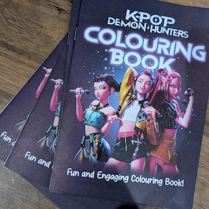 Op de afbeelding: Verschillende exemplaren van een kleurboek getiteld "KPOP Demon Hunters Colouring Book" liggen op een houten oppervlak. De cover toont drie geanimeerde figuren met microfoons. De tekst "Fun and Engaging Colouring Book!" is ook zichtbaar.