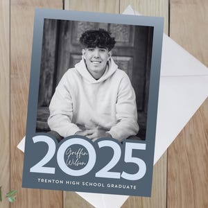 May include: A graduation announcement card with a blue background and white text. The card features a photo of a young person in a white hoodie and the text "2025" with a circle containing the name "Griffin Wilson" in white text. The text "Trenton High School Graduate" is at the bottom of the card.
