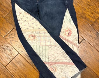 May include: Dark blue denim jeans with patchwork fabric panels down the sides. The patchwork features floral and geometric patterns in shades of pink, cream, and green. The jeans have a classic five-pocket design.
