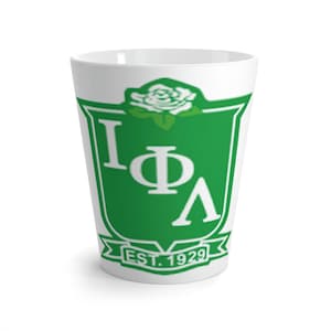 Può includere: Tazza in ceramica bianca con uno stemma verde e bianco che presenta le lettere "IΦA" e il testo "EST. 1929". Una rosa bianca è sopra lo stemma.