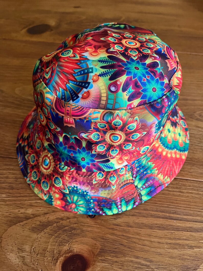 Puede incluir: Un sombrero de pescador colorido con un patr&oacute;n psicod&eacute;lico de flores y remolinos en tonos de rojo, naranja, amarillo, azul, verde y morado.