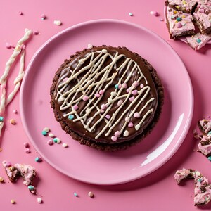 May include: A chocolate tart with white chocolate drizzle and colourful sprinkles on a pink plate. The tart is surrounded by more sprinkles and other chocolate treats.