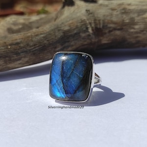 Könnte beinhalten: Ein silberner Ring mit einem quadratischen blauen Labradorit-Edelstein. Der Ring liegt auf einer weißen Oberfläche.