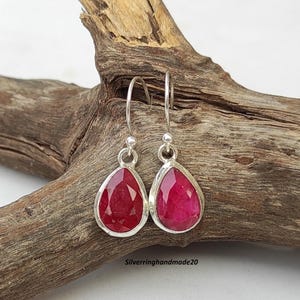 Puede incluir: Pendientes colgantes de plata con piedras preciosas de rubí facetadas en forma de lágrima. Los pendientes tienen un diseño sencillo con un engaste de bisel plateado y un cierre de gancho. Las piedras de rubí son de color rojo intenso.