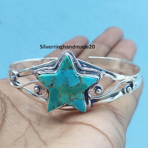 May include: A silver cuff bracelet featuring a central star-shaped turquoise stone with brown matrix patterns. The metal band displays decorative swirling wire details on both sides of the star. The text Silverringhandmade20 is visible.