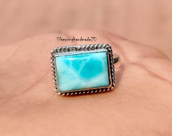 May include: A silver ring featuring a blue and white gemstone set in a rectangular bezel. The ring has a rope-like design around the bezel.