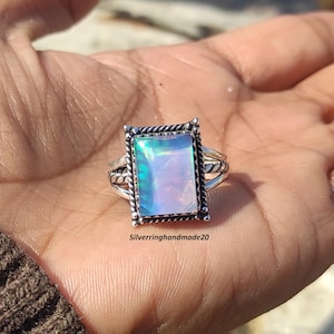 May include: A silver ring with a rectangular iridescent opal gemstone set in a silver frame. The ring has a twisted silver band.