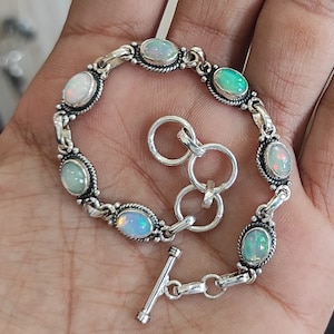 Peut inclure: Un bracelet en argent avec un fermoir à glissière présente des pierres précieuses d'opale de forme ovale serties dans des chatons en argent. Le bracelet a un design de chaîne délicat.