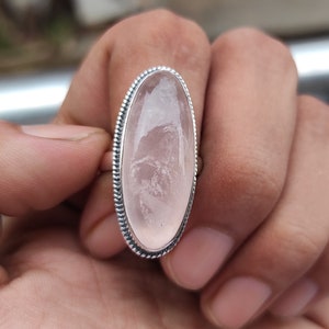 May include: A silver ring with a large oval-shaped pink rose quartz gemstone.
