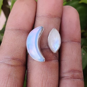 May include: A silver ring with a crescent moon and teardrop shaped moonstone. The ring is on a person's finger.