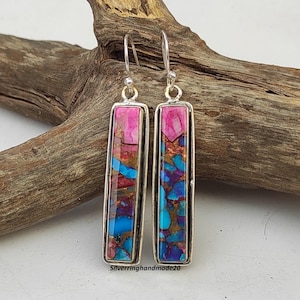May include: A pair of silver dangle earrings featuring rectangular turquoise and pink stone accents. The stones have a marbled pattern with shades of blue, pink, and brown.