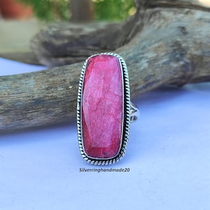 Puede incluir: Un anillo de plata con una gran piedra preciosa rectangular de color rosa. El anillo tiene un diseño de cuerda alrededor del borde del engaste.