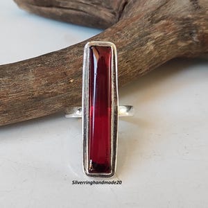 May include: A silver ring with a rectangular red gemstone. The ring is set in a simple, modern style.