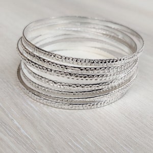 Puede incluir: Un conjunto de pulseras de plata con textura martillada. Las pulseras están apiladas unas sobre otras.