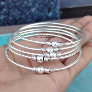 May include: Five silver bangles with a small ball charm on each. The bangles are stacked on top of each other.
