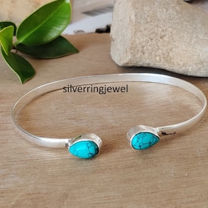 Puede incluir: Un brazalete de plata con dos piedras turquesa en forma de lágrima. El brazalete es abierto y ajustable.