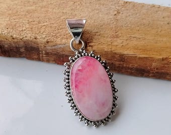May include: A pink and white oval gemstone pendant with a silver setting. The pendant has a detailed, scalloped edge.