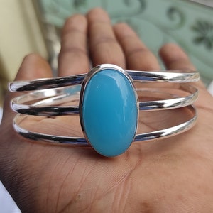 May include: A silver bangle bracelet with three bands and a large oval-shaped light blue gemstone.