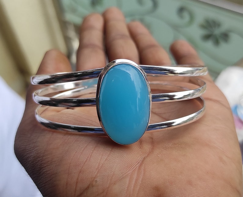 May include: A silver bangle bracelet with three bands and a large oval-shaped light blue gemstone.